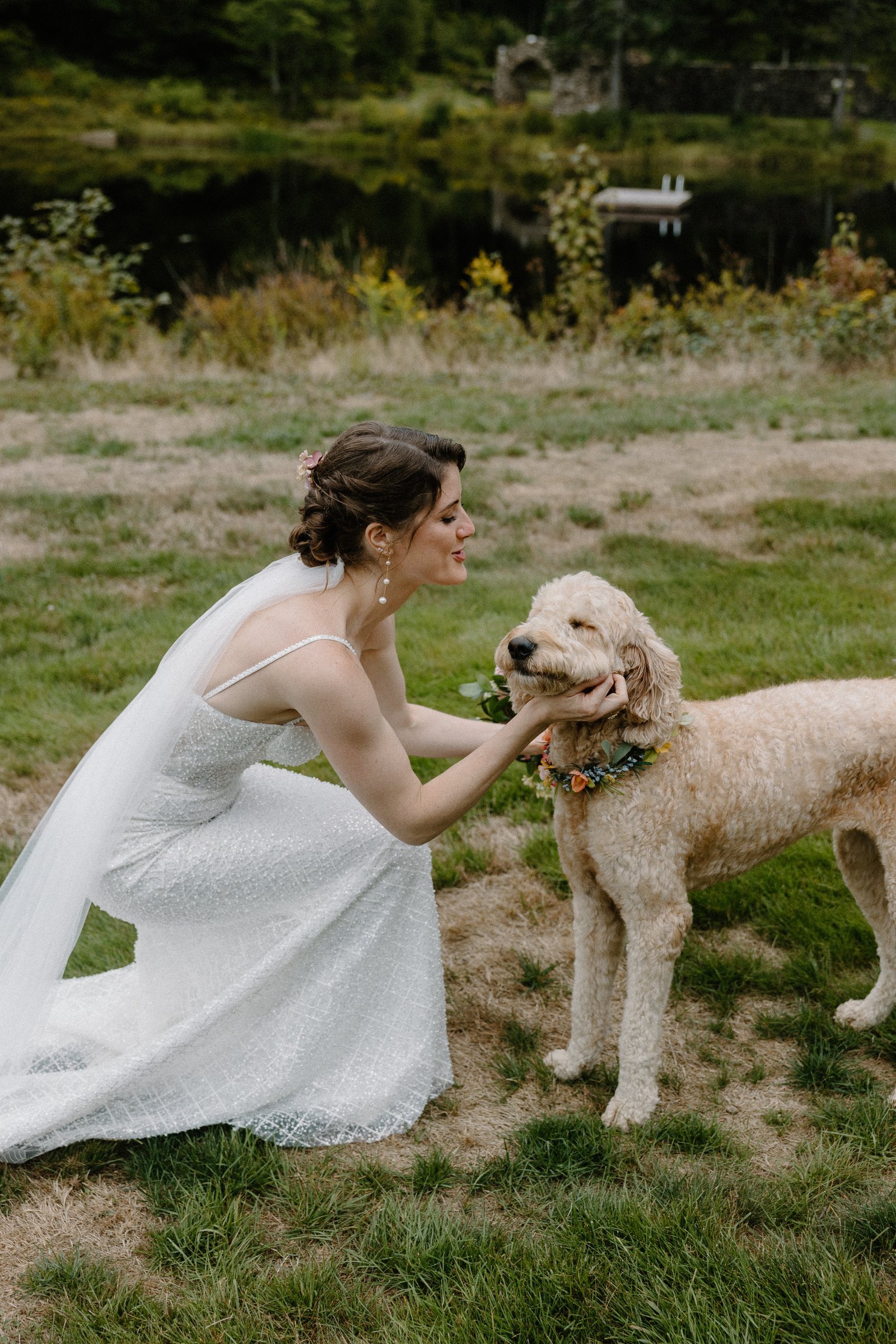 The bride kneeling to greet the dog on the lawn